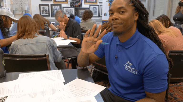 John smiles and waves to the camera at a workshop hosted by Free Minds Book Club & Writing Workshop